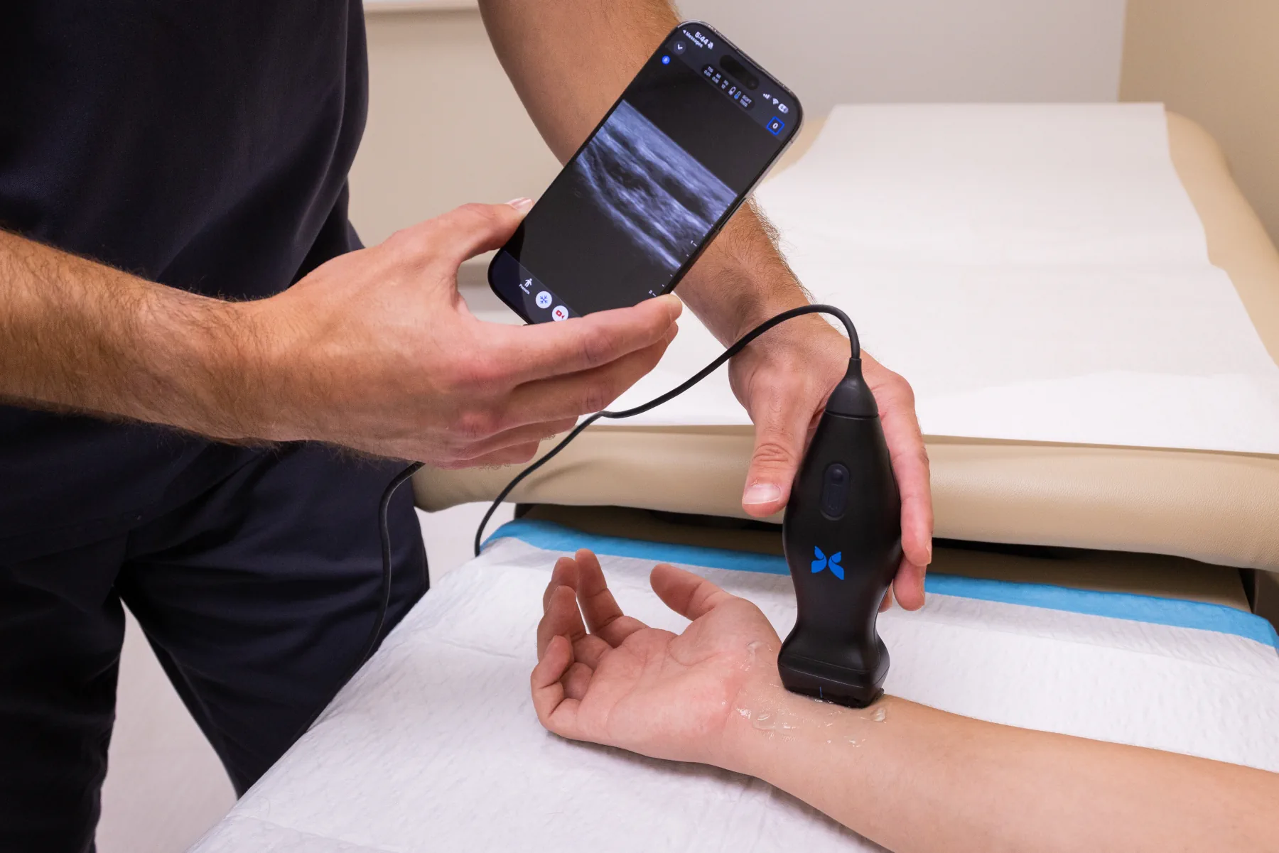 Clineva clinician using a handheld ultrasound probe on a patient's wrist while reviewing the scan on a phone